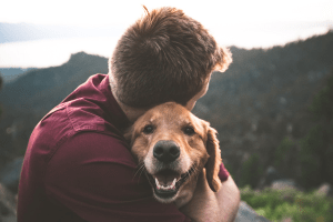 Person hugging a dog, forested mountains in the background